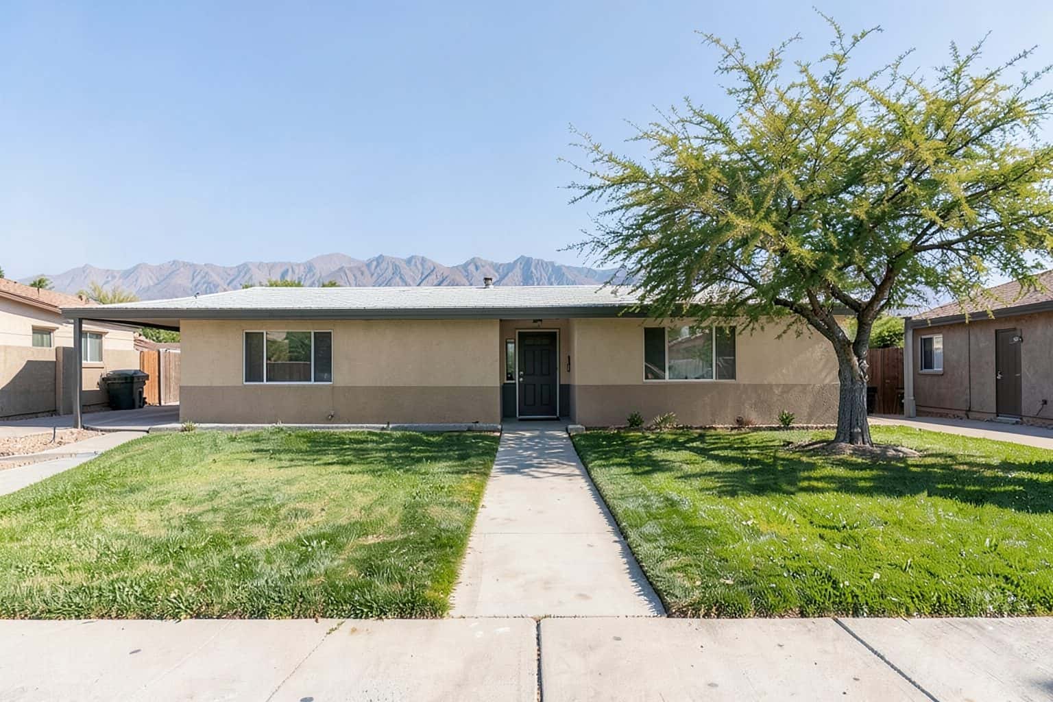 Sample yard: a single-story ranch house with a walkway between two lawns and mountains behind